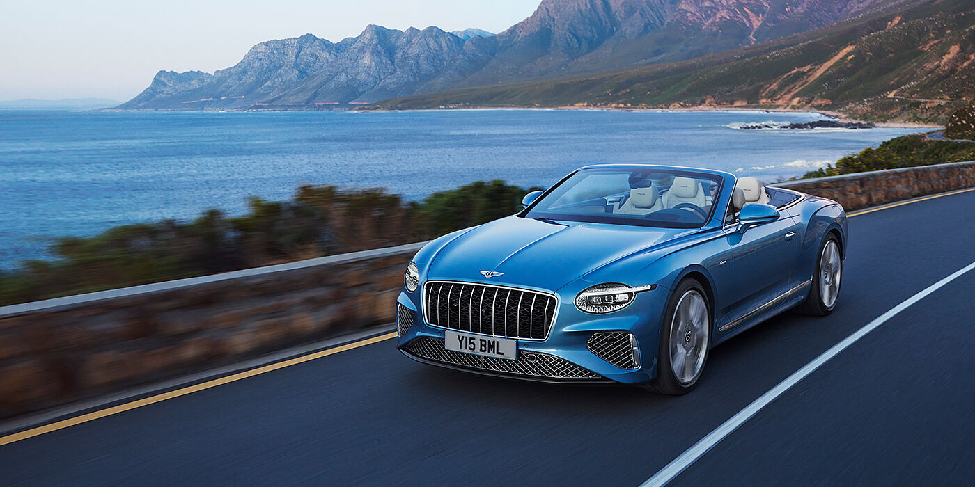 Bentley Hatfield New Bentley Continental GTC Azure convertible in Light Windsor blue paint with 22 inch Azure wheels and chrome grill, driving dynamically by the sea