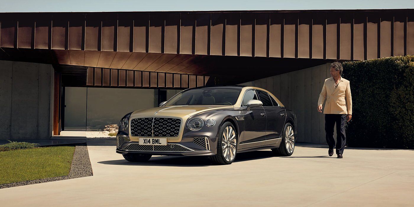 Bentley Hatfield Bentley New Flying Spur Mulliner V8 hybrid sedan front three quarters in Rose Gold over Magnetic paint, parked near modern home