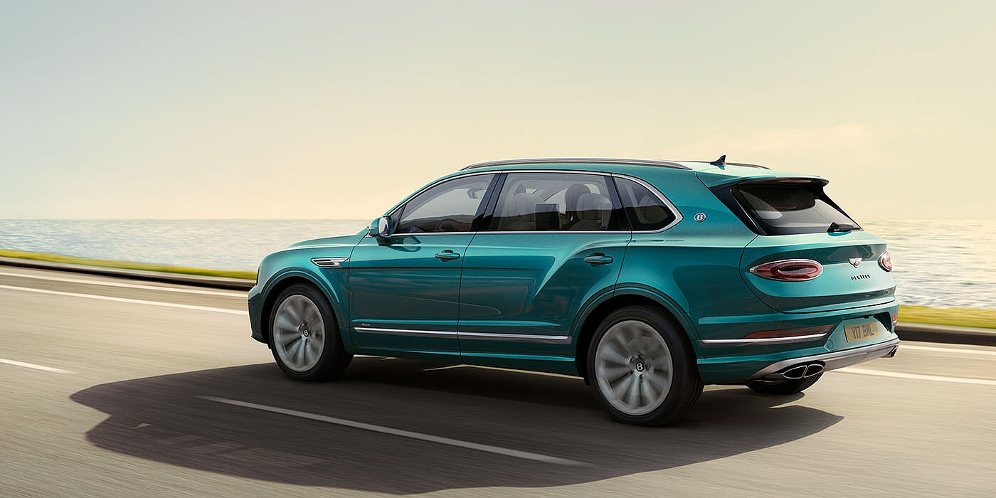 Bentley Hatfield Bentley Bentayga Extended Wheelbase Azure luxury SUV rear three quarter in Topaz Blue by Mulliner paint, driving on an ocean road.