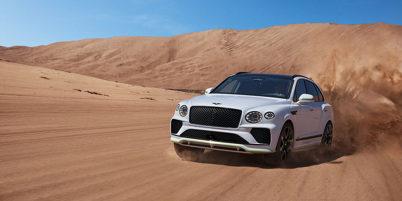 Bentley Hatfield Bentley Bentayga Speed SUV front three quarter in Snow Quarts Pearlescent by Mulliner white paint driving dynamically through the desert