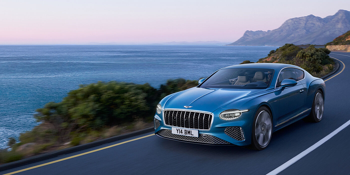 Bentley Hatfield New Bentley Continental GT Azure coupe in Light Windsor blue paint with 22 inch Azure wheels and chrome grill, driving dynamically by the sea