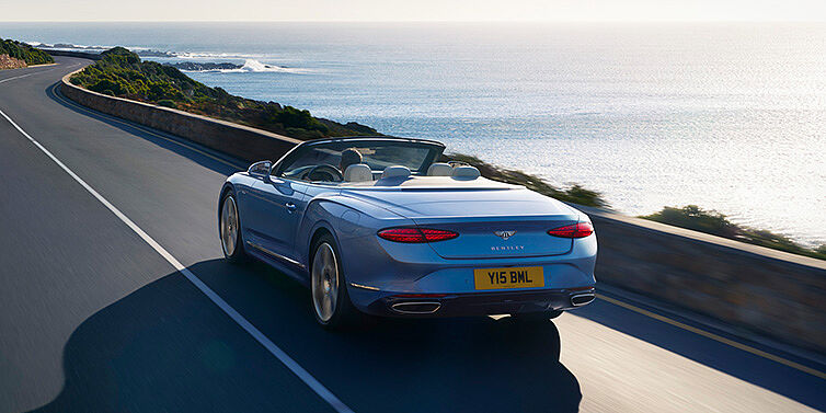 Bentley Hatfield New Bentley Continental GTC Azure convertible rear view in Light Windsor blue paint with 22 inch ten spoke wheels driving dynamically on an ocean road in the sunshine