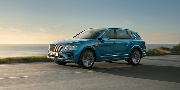 Bentley Hatfield Bentley Bentayga Azure SUV in Topaz blue paint driving dynamically by the ocean with 22 inch 10 spoke directional wheels