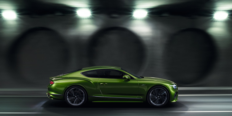 Bentley Hatfield Bentley Continental GT Speed coupe profile in Tourmaline Green driving dynamically past a concrete wall at night