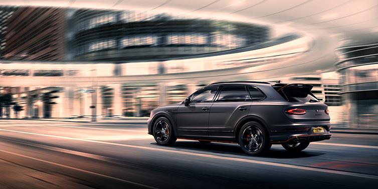 Bentley Hatfield Bentley Bentayga S Black Edition SUV rear three quarter in Anthracite Satin paint driving dynamically through a city at night