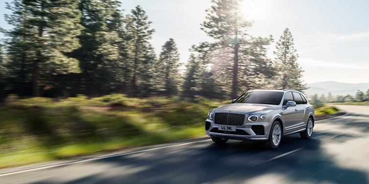 Bentley Hatfield Bentley Bentayga SUV front three quarter in Moonbeam silver paint driving dynamically along a tree-lined road