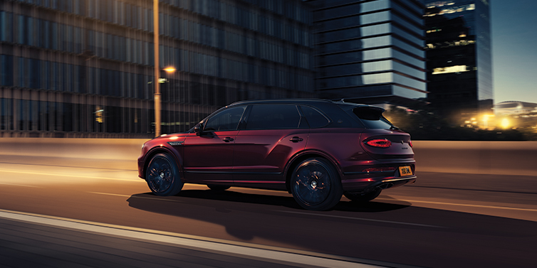 Bentley Hatfield Bentley Bentayga Extended Wheelbase Mulliner SUV in Cricket Ball red paint driving dynamically in city at night