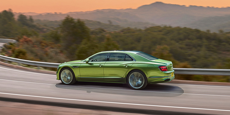 Bentley Hatfield Bentley Flying Spur Speed sedan side profile in Tourmaline Green paint driving dynamically on a mountain road at sunset