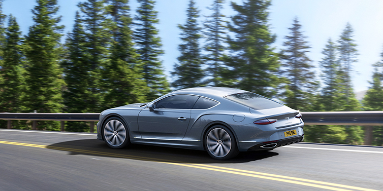 Bentley Hatfield New Bentley Continental GT coupe in Silverlake paint, seen from the rear, driving dynamically on a tree-lined road