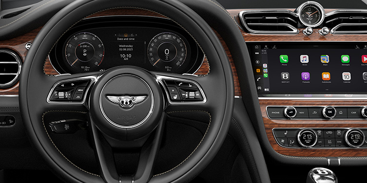 Bentley Hatfield Bentley Bentayga SUV front interior detail of steering wheel and driver screens surrounded by Beluga black hide and Crown Cut Walnut veneer